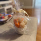 Floral candle bouquet — orange & ivory flowers, gift-wrapped in clear cellophane with cream ribbon