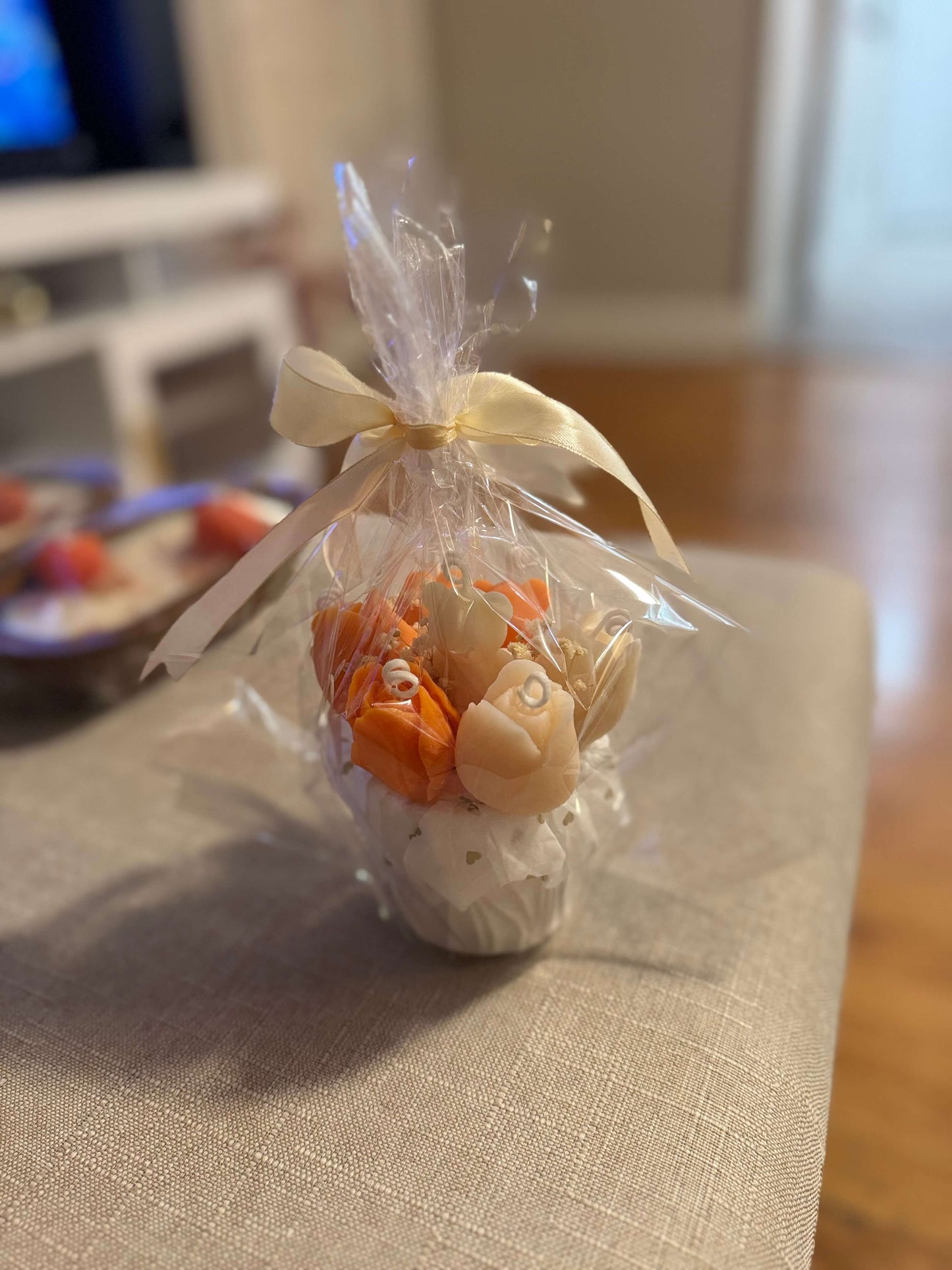 Floral candle bouquet — orange & ivory flowers, gift-wrapped in clear cellophane with cream ribbon