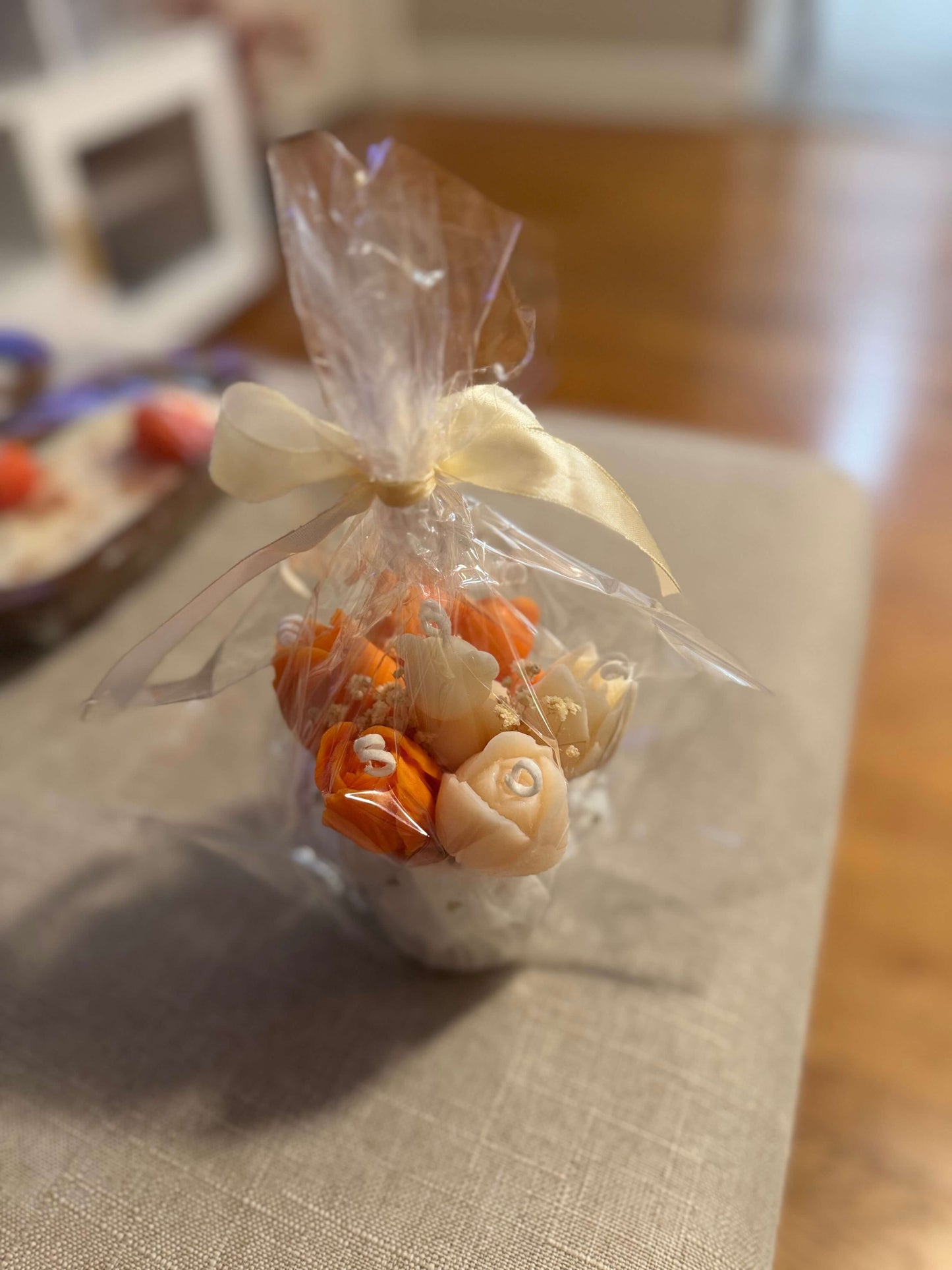Floral candle bouquet — orange & ivory flowers, gift-wrapped in clear cellophane with cream ribbon
