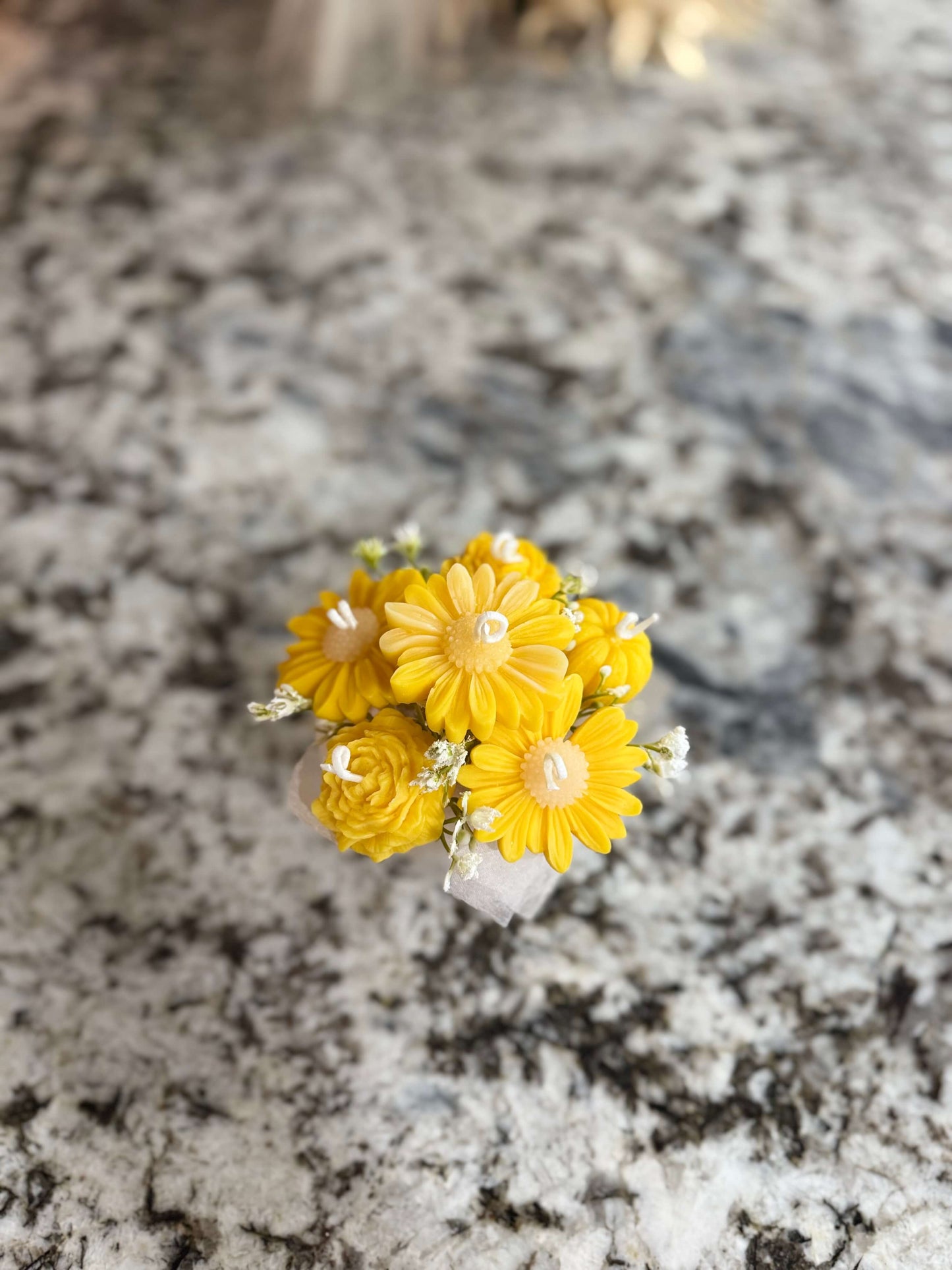 Small bouquet of yellow flowers in a white vase on a marble countertop